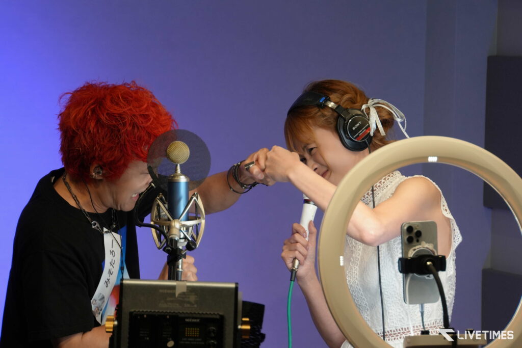 Two people in a recording studio high-fiving over a microphone setup, blue background behind them.