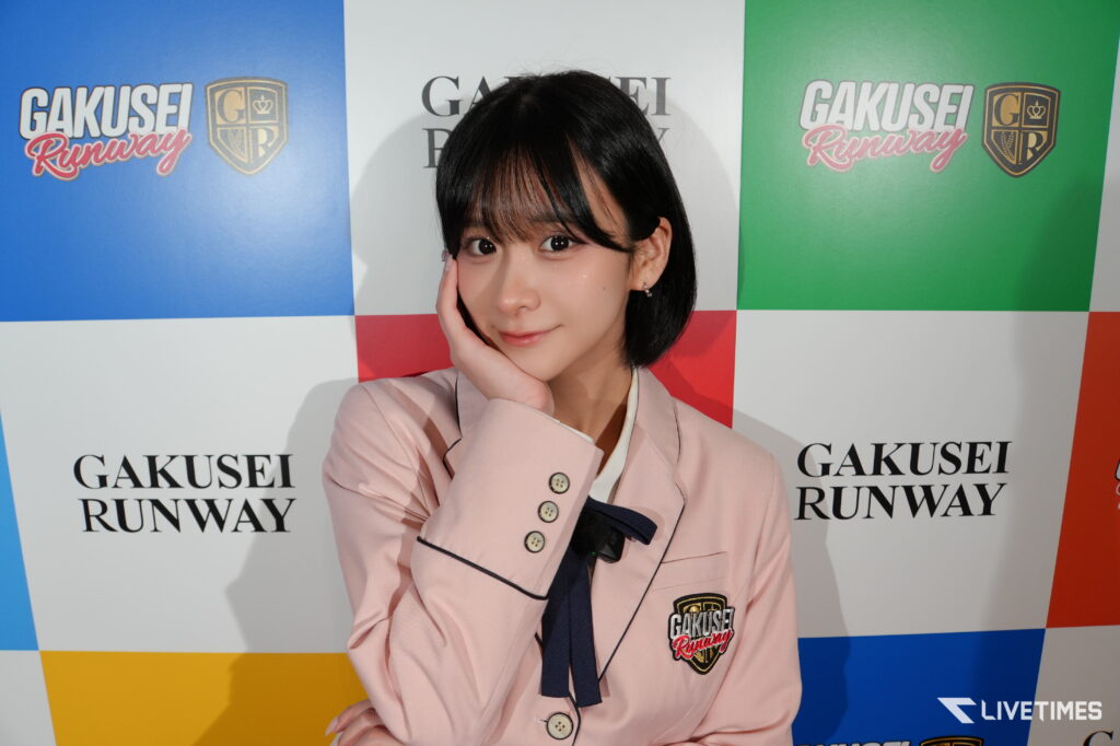 Woman posing with her hand on her cheek in a pink blazer, in front of a multicolor backdrop that reads GAKUSEI RUNWAY.