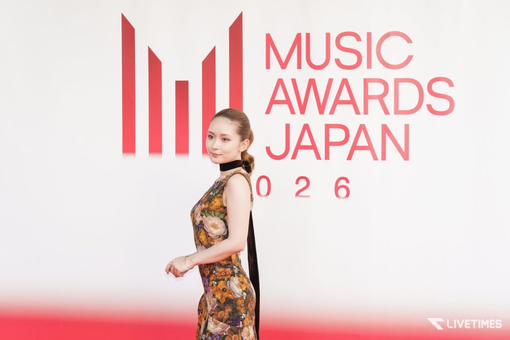 Woman in a floral, sleeveless dress posing on a red carpet in front of a backdrop that reads 'MUSIC AWARDS JAPAN'.] ,