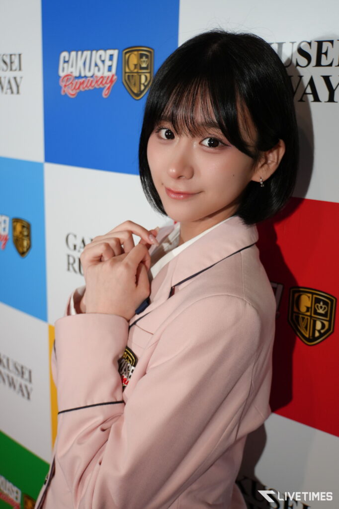 Young woman in a pale pink blazer posing at a fashion event with a blue and white backdrop reading 'GAKUSEI RUNWAY'.
