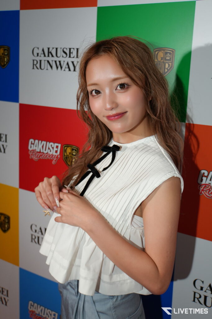 Young woman posing in front of a colorful backdrop with Gakusei Runway logos at an event.