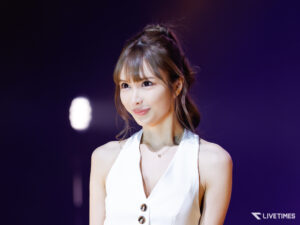 Close-up of a female performer in a white sleeveless dress on stage with a dark purple background, LIVETIME logo visible bottom-right.