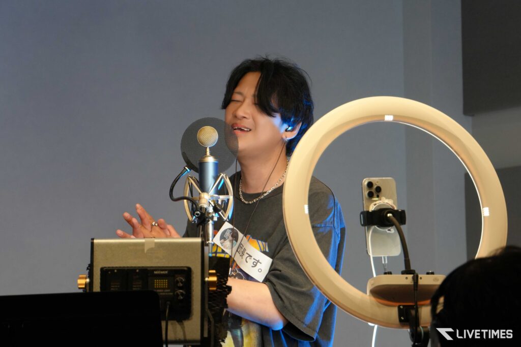 A singer wearing a headset performs into a microphone with a pop filter in a studio, ring light glowing nearby.