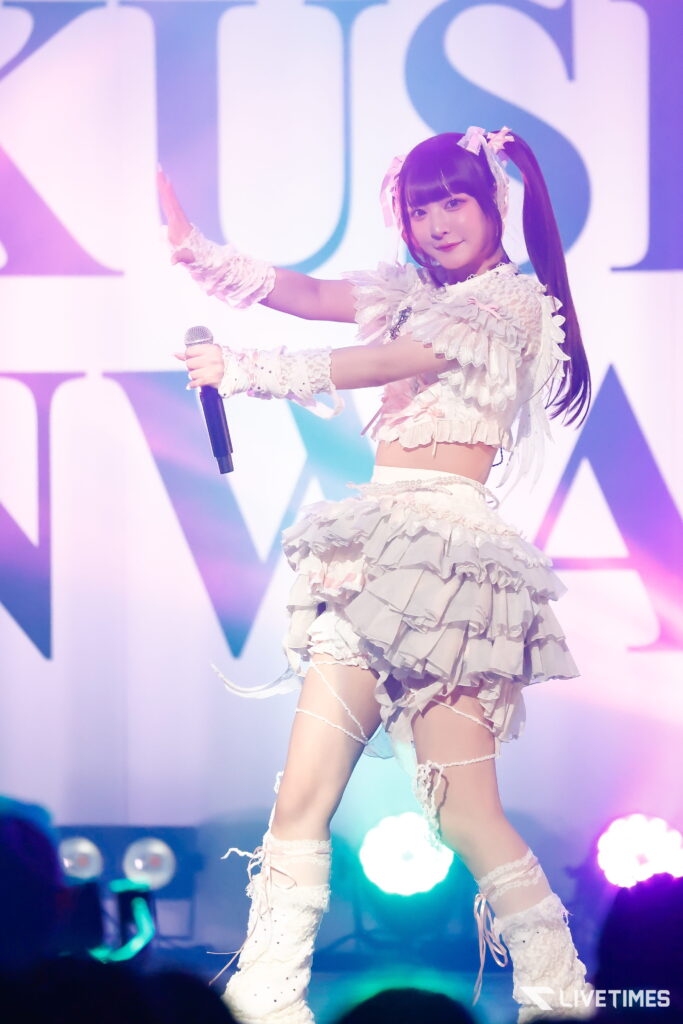 Young female singer in a white ruffled stage costume holding a microphone during a performance.