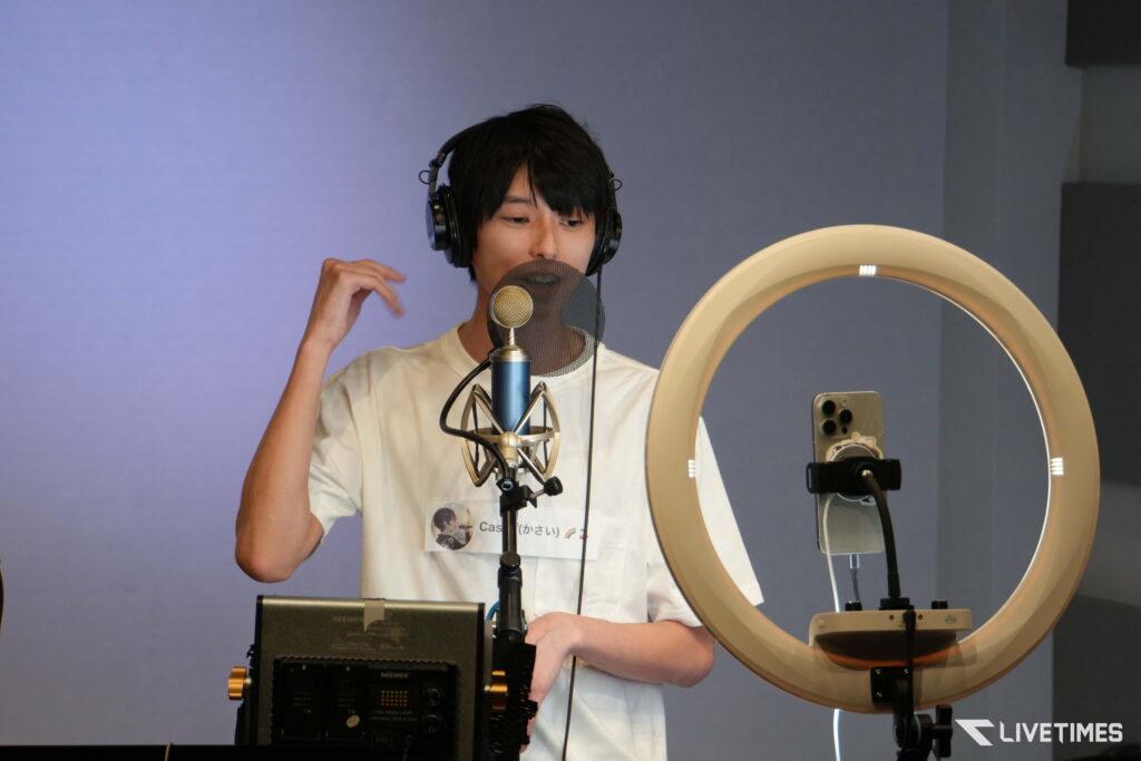 Young man wearing headphones speaks into a studio microphone with a pop filter in a recording setup.