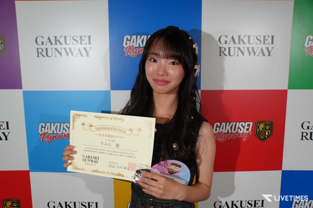 Young woman smiles while holding a certificate at a Gakusei Runway event backdrop.