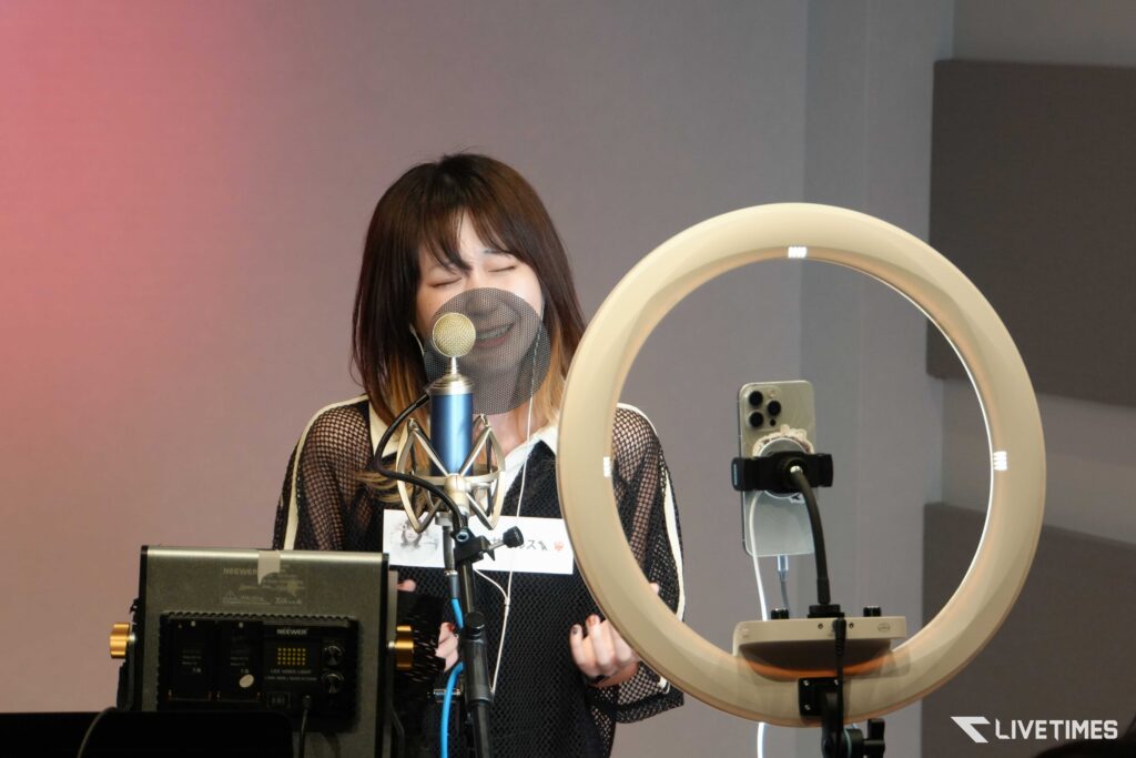Woman singing into a studio microphone with a pop filter, ring light in the foreground