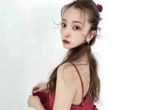 Portrait of a young woman in a red spaghetti-strap dress, looking over her shoulder against a white background.