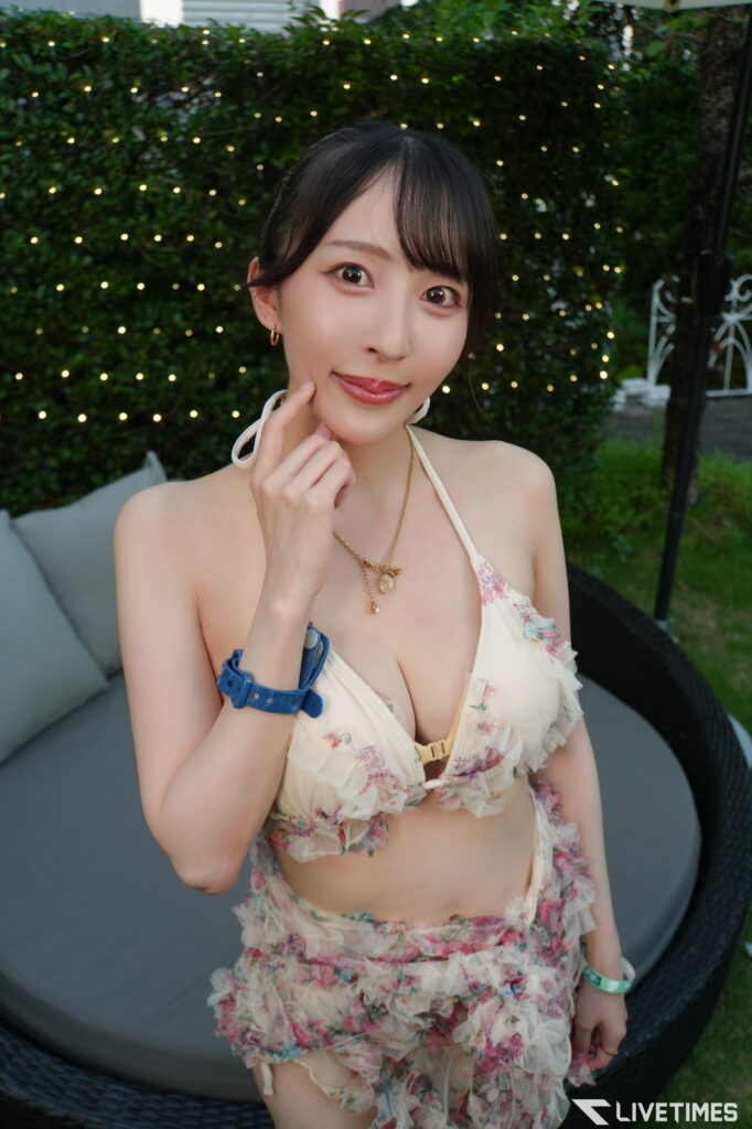 Woman in a floral strapless swimsuit top posing outdoors, touching her chin with fairy lights and greenery behind her.