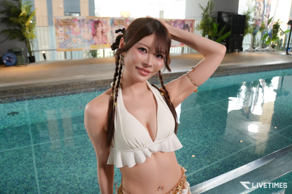 Portrait of a woman in a white bikini by an indoor pool, her hand resting on her head and braided hair