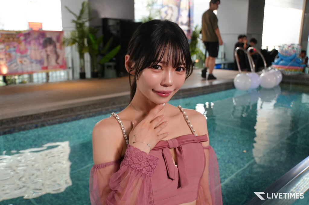 Portrait of a smiling young woman in a pink dress posing by an indoor pool at an event location.