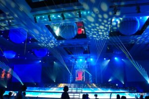 Stage set with blue lighting, laser beams, and a red ornate throne at center.
