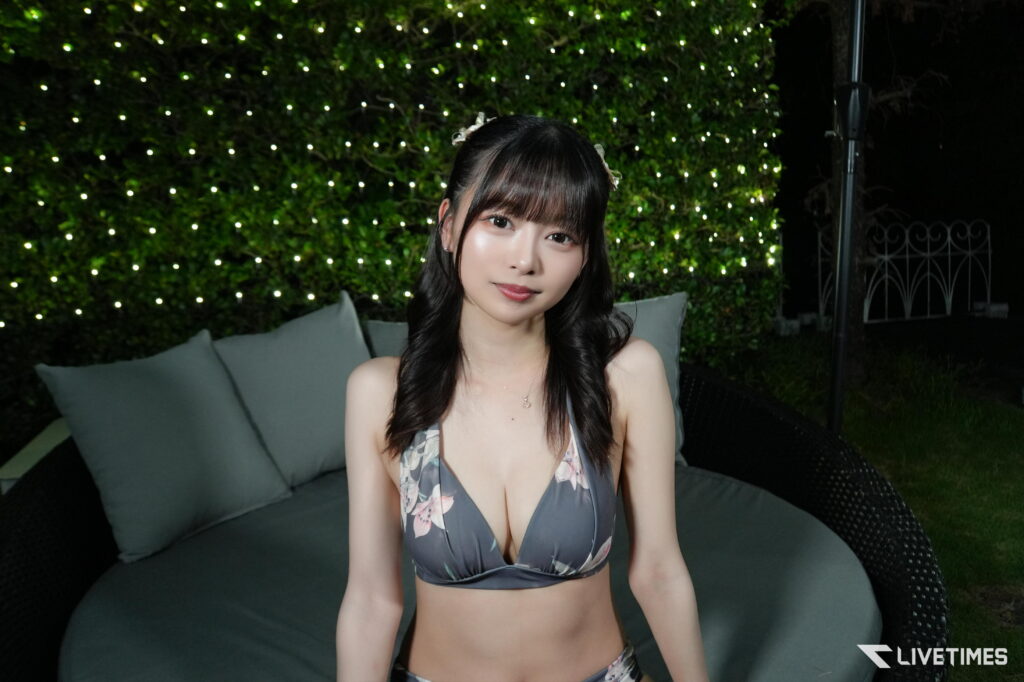 Young woman in a floral bikini top sits on a couch outdoors at night with string lights behind her.
