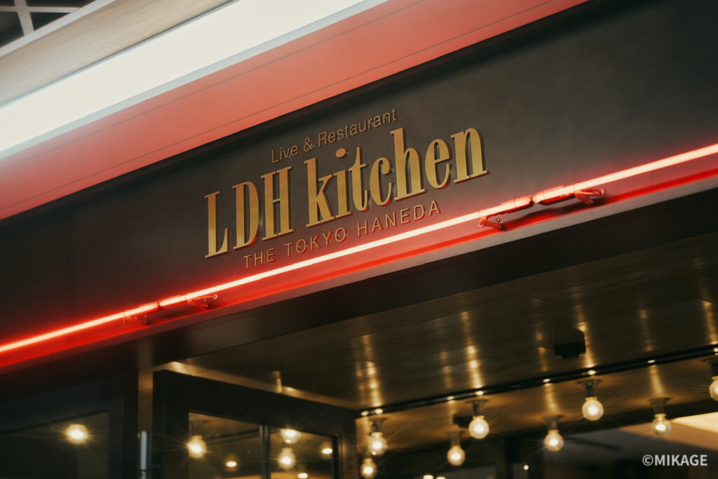 Storefront sign reading 'LDH Kitchen' with 'Live & Restaurant' and 'The Tokyo Haneda' beneath, illuminated by red neon lights.
