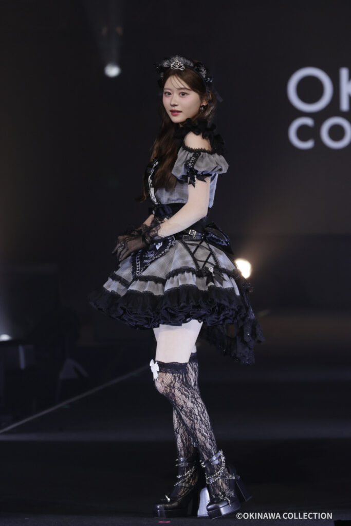 Gothic lolita fashion model posing on a dark stage in a gray and black frilly dress with gloves and headpiece
