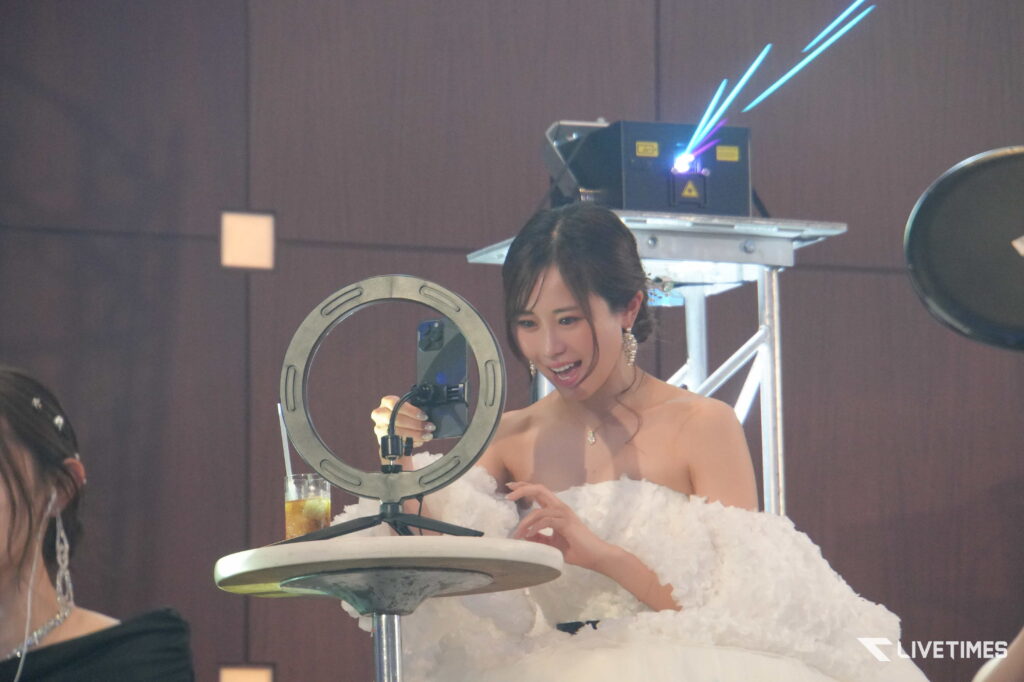 Woman in a white wedding dress operating a laser or light device at an event, with blue laser beams visible in the background.