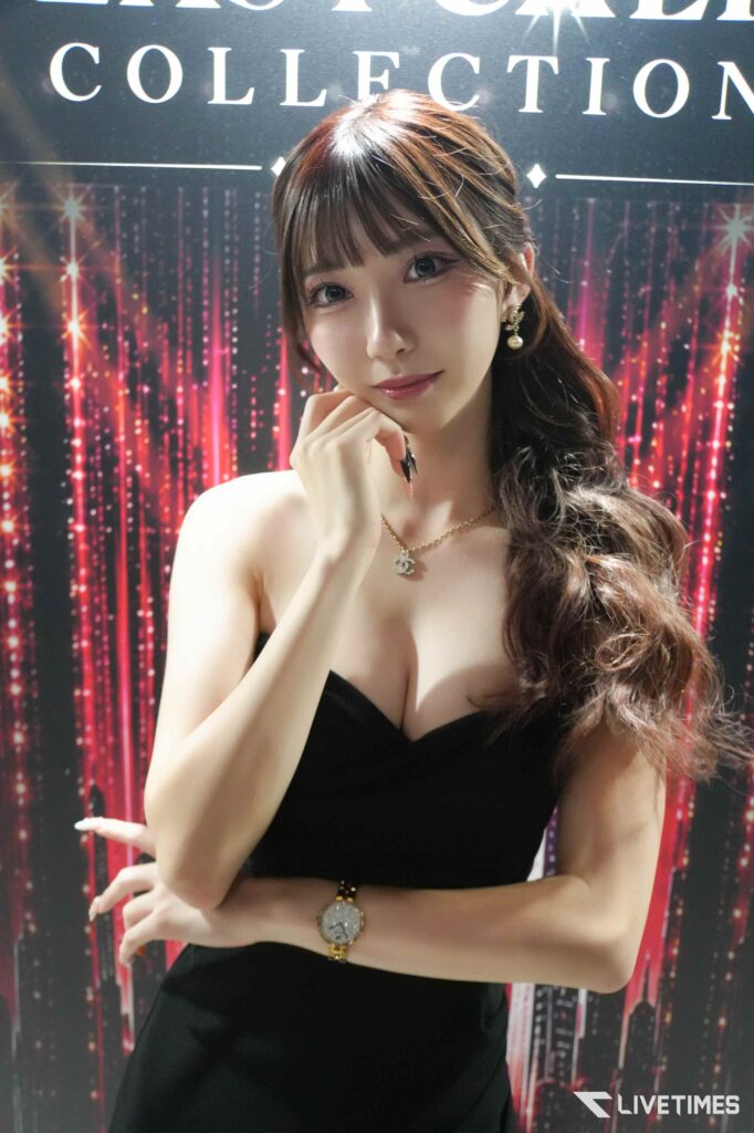 Young woman in a black strapless top posing with her hand under her chin against a sparkly backdrop.