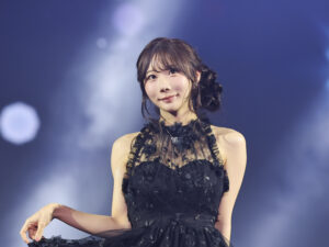 Young woman in a black lace dress smiling on stage with blue lights in the background