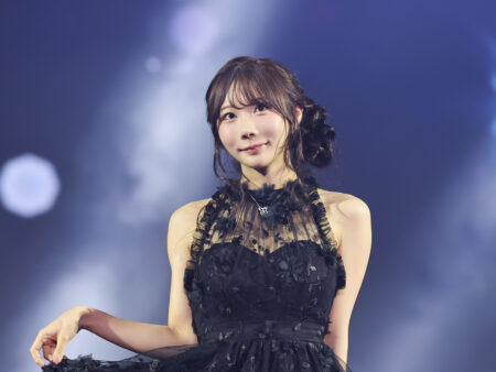 Young woman in a black lace dress smiling on stage with blue lights in the background