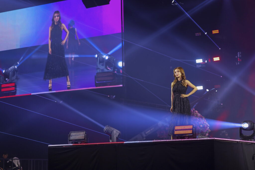 Two female performers in elegant black gowns on a lit stage with purple-blue lights and lasers.
