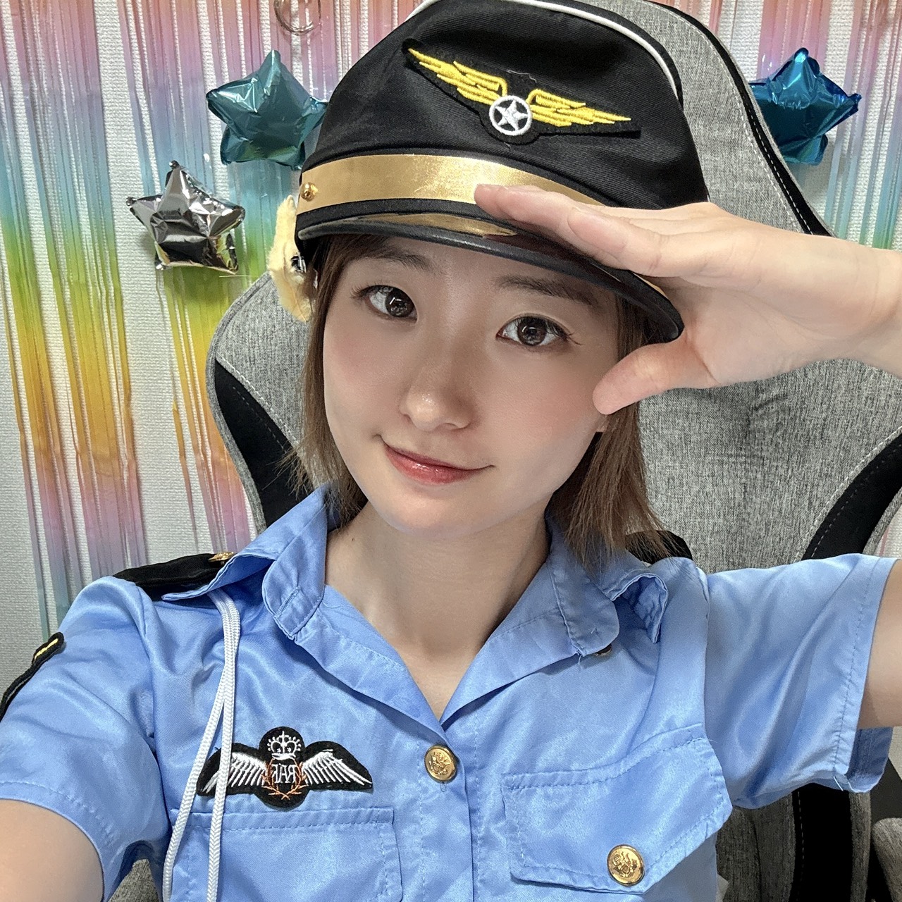 Young woman in a light blue pilot uniform, saluting while wearing a captain's hat with a gold band and wing badge.