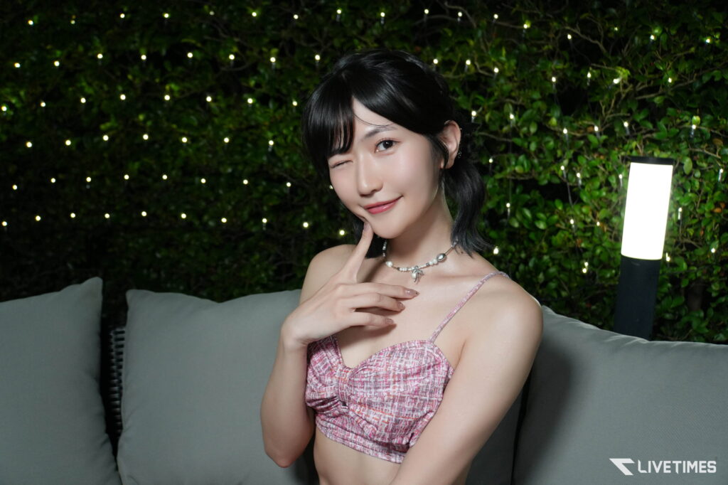 Smiling woman in a pink patterned top posing on an outdoor sofa with string lights in the background.