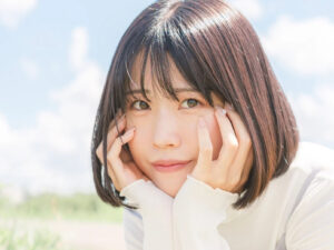 人気ライバー・あいちゃん、楽天イーグルスの始球式に出演決定。2年越しのPococha始球式イベントで悲願の1位 Close-up of a young woman resting her face in her hands outdoors on a sunny day with a blue sky behind her in a soft, natural portrait.