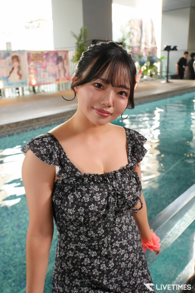 Young woman in a black floral dress posing by an indoor pool, smiling at the camera.