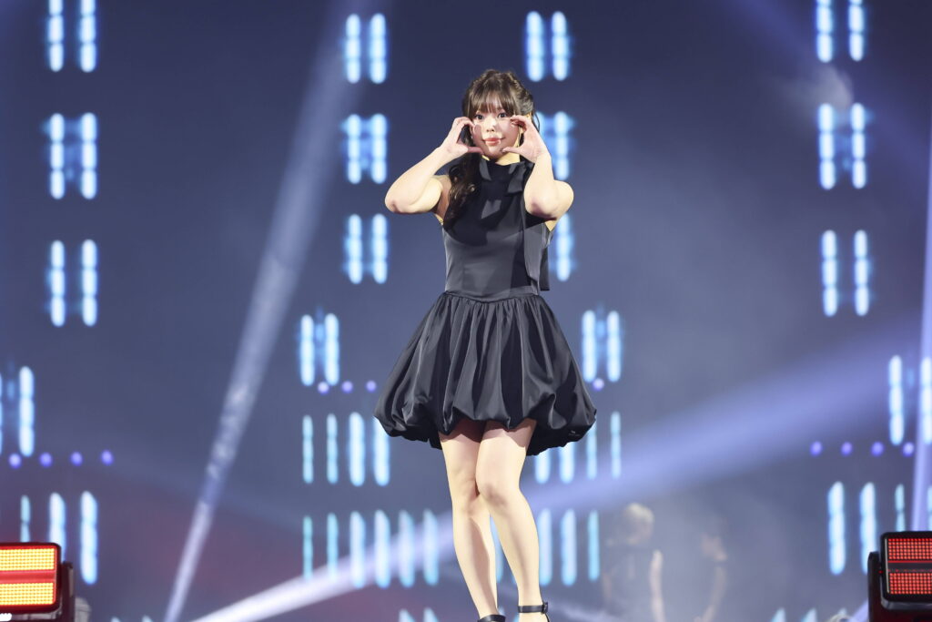 Female performer in a black dress on stage, hands framing her face amid blue stage lights