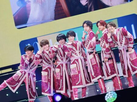 Eight performers in matching pink glittery outfits posing on stage during a concert.','K-pop group in coordinated pink costumes posing with finger guns on stage.','Group photo of a boy band in sparkling pink stage outfits, smiling at camera.','Eight-member stage performance wearing sequined pink uniforms with white belts.