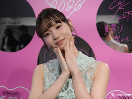 Portrait of a young woman with hands folded near her face, wearing a lace dress, against a pink backdrop with event graphics.