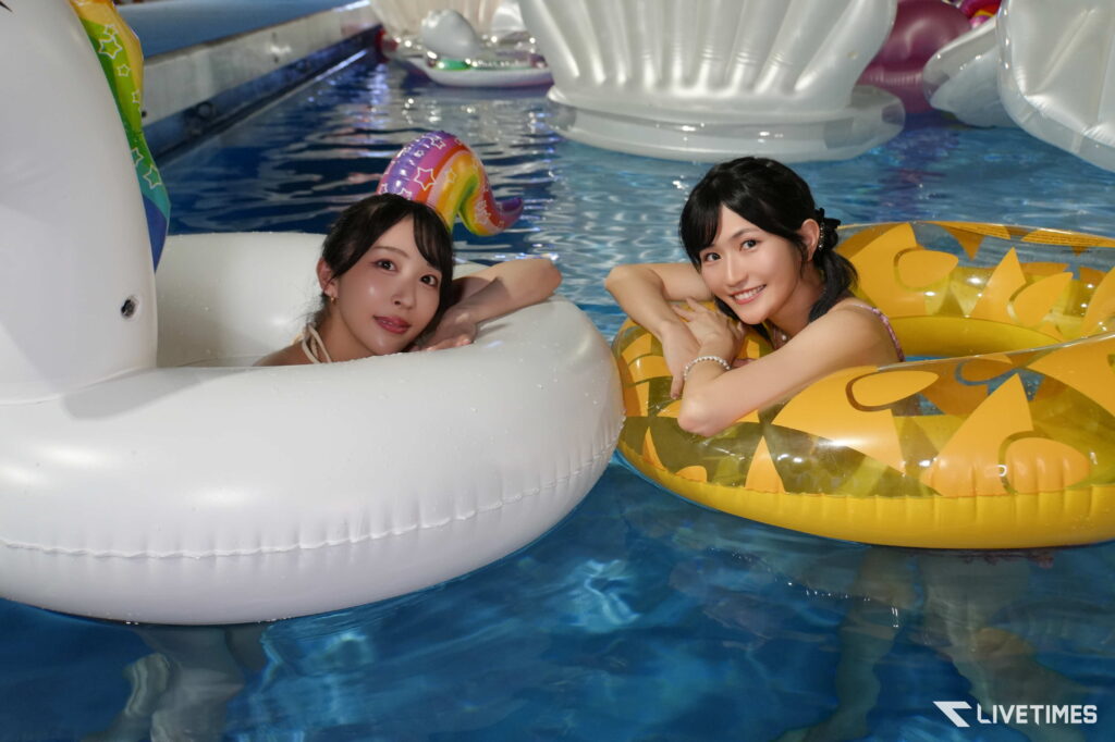 Two young women relaxing in inflatable pool tubes in a lazy-water setting, smiling at the camera.
