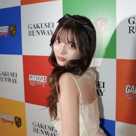 Young woman posing at a fashion event with a colorful backdrop displaying 'GAKUSEI RUNWAY' text and logos