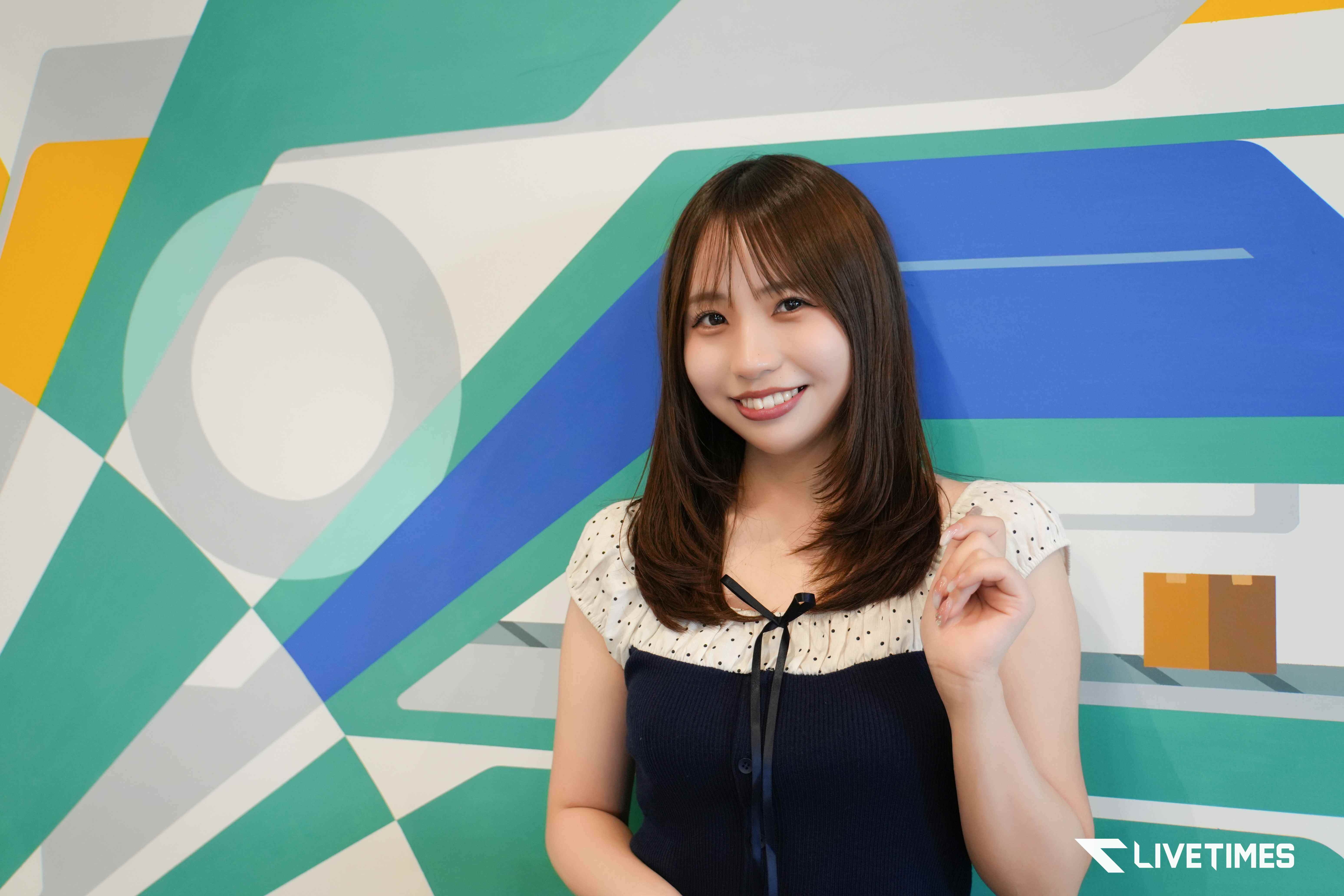Smiling young woman posing against a bright geometric mural with teal, blue, and yellow shapes.