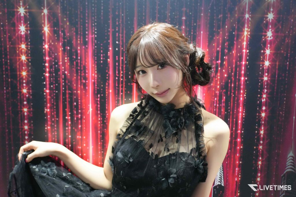 Young woman in a black lace dress posing against a pink glitter backdrop.