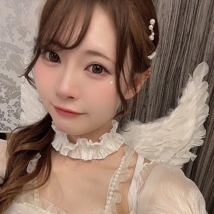 Young woman in a white angel costume with feathered wings and pearl hair accessories, smiling at the camera.