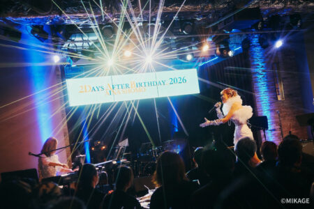 Live concert scene: a female singer in a white dress performs on stage with a pianist, blue lighting and starburst beams, and a banner behind reading '2 Days After Birthday 2026'.