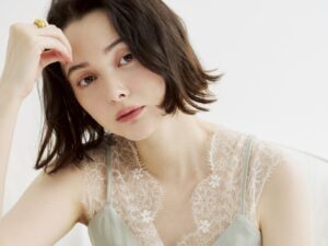Close-up portrait of a young woman with short brown hair, wearing a lace top and pale green dress, looking to the side.