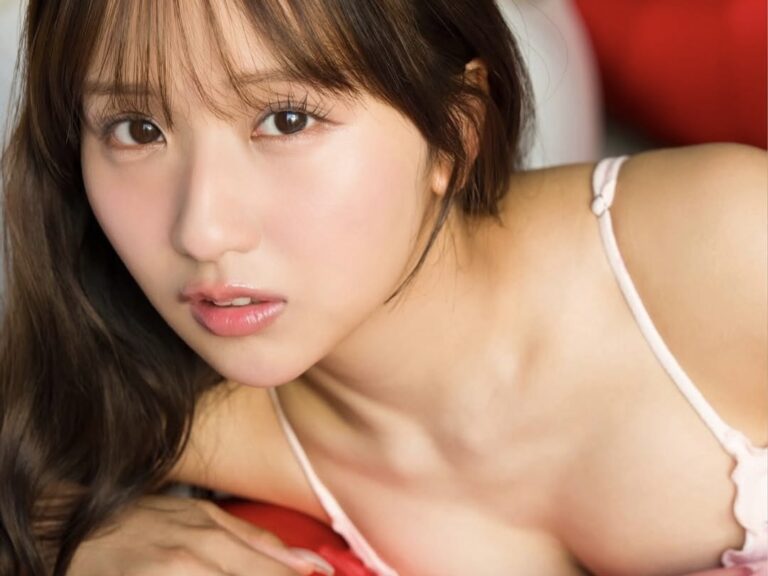 Close-up portrait of a young woman with long hair, wearing a light pink spaghetti-strap top, looking toward the camera with a soft expression.
