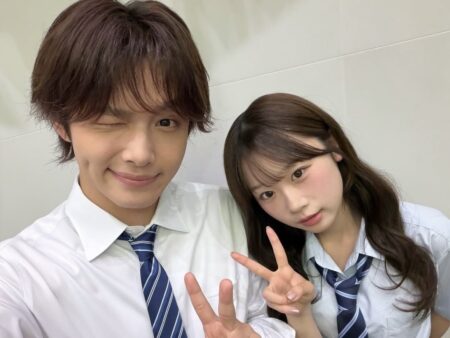 Two students in white shirts and striped ties pose for a selfie, flashing peace signs at the camera.
