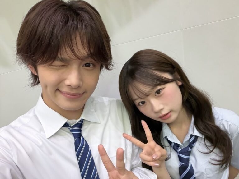 Two students in white shirts and striped ties pose for a selfie, flashing peace signs at the camera.