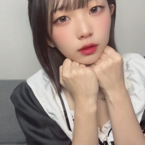 Young woman in a black-and-white maid outfit with cat-ear headband, resting her chin on her hands in a cosplay pose.