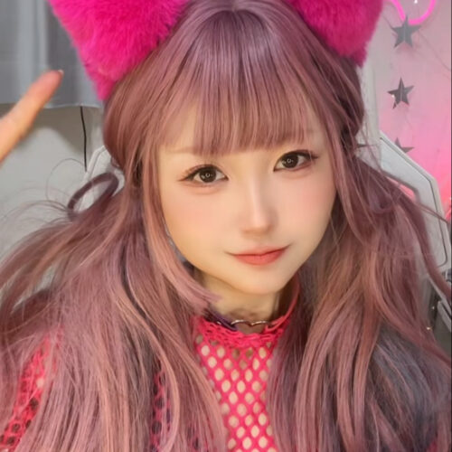 Young woman with pastel pink-purple hair wearing bright pink fluffy cat-ear headband, pink mesh top and purple shirt in a neon-styled setting.