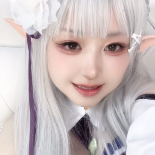 Self-portrait of a cosplayer with silver hair, elf ears, a large white flower headpiece, and a blue-white costume.