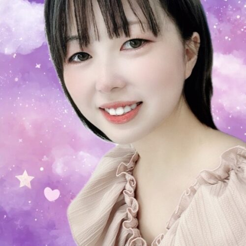 Portrait of a smiling young woman with dark hair and bangs, wearing a beige ruffled top, against a purple starry backdrop with hearts.