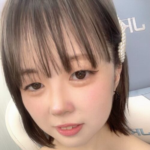 Close-up portrait of a young woman with short brown hair and bangs, wearing a pearl hair clip and subtle makeup.